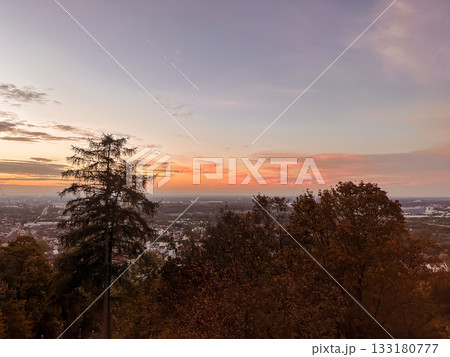 Scenic sunset view from a hilltop with vibrant colors illuminating the sky, silhouetting trees and showcasing a panoramic landscape below Scenic sunset view from a hilltop with vibrant colors illuminating the sky, silhouetting trees and showcasing a panoramic landscape below 133180777