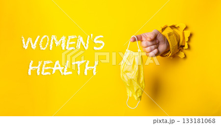 Hand holding a yellow mask with the words womens health written below it 133181068