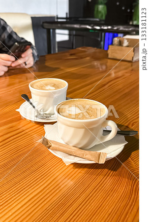 Two cups of coffee on a wooden table with a cozy atmosphere, showcasing rich textures and warm tones, perfect for a coffee shop or cafe setting Two cups of coffee on a wooden table with a cozy atmosphere, showcasing rich textures and warm tones, perfect for a coffee shop or cafe setting 133181123