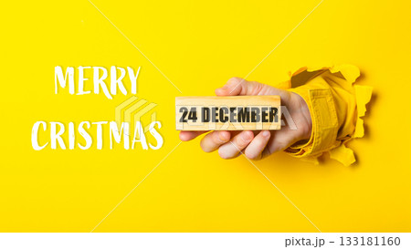 Hand holding wooden block with date 24 December, surrounded by festive Merry Christmas text Hand holding wooden block with date 24 December, surrounded by festive Merry Christmas text 133181160