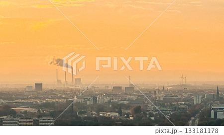 Industrial skyline at sunset with smoke stacks and wind turbines in a hazy atmosphere Industrial skyline at sunset with smoke stacks and wind turbines in a hazy atmosphere 133181178