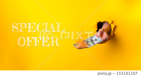 Hand holding cash emerging from a torn yellow background with promotional text for special offer 133181187