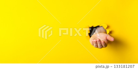 Hand emerging from a torn yellow wall, symbolizing creativity and breaking barriers in design 133181207