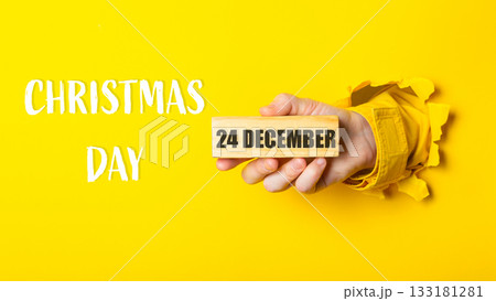 Hand holding wooden block with date 24 December, celebrating Christmas Day with vibrant yellow background Hand holding wooden block with date 24 December, celebrating Christmas Day with vibrant yellow background 133181281