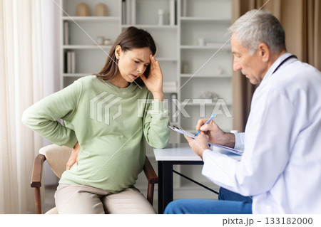 Pregnant woman suffering headache having appointment with senior doctor in clinic Pregnant woman suffering headache having appointment with senior doctor in clinic 133182000