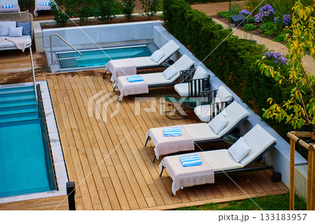 Outdoor pool area with lounge chairs and towels on wooden deck in hotel 133183957