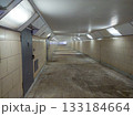A long underground corridor with fluorescent lights, beige tiled walls and metal doors. 133184664