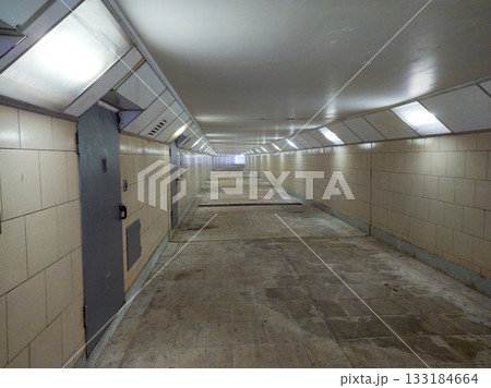 A long underground corridor with fluorescent lights, beige tiled walls and metal doors. 133184664