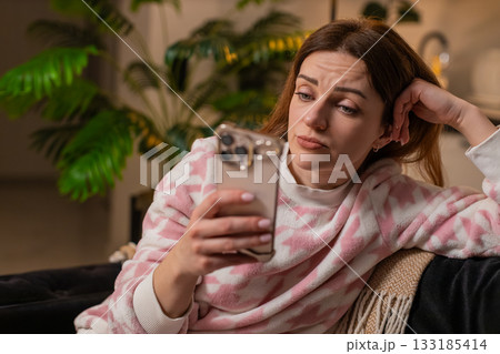 Adult woman scrolls phone news at night boredom sets in tired eyes stress demotivation sighs frowns 133185414