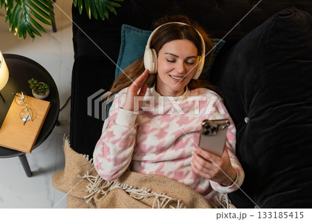 Adult woman with wireless headphones listens to music on smartphone eyes closed nods smiles gently 133185415