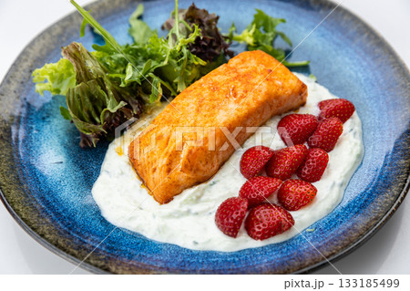 Seared salmon fillet with yogurt sauce, fresh strawberries and greens on blue ceramic plate 133185499