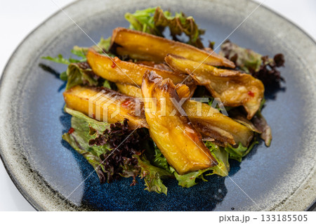 Roasted eggplant salad with sweet chili glaze on mixed greens, overhead on ceramic plate 133185505