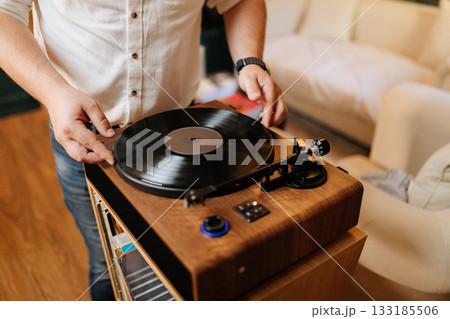 Placing a vinyl record on a wooden turntable at home, cozy audiophile moment Placing a vinyl record on a wooden turntable at home, cozy audiophile moment 133185506