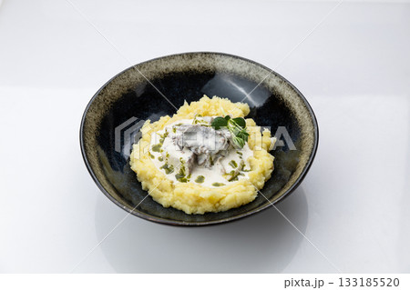 Mashed potatoes with creamy mushroom sauce in black bowl, minimal white background, top view 133185520