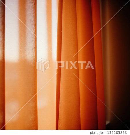 Red curtains hang gracefully beside a window, allowing soft morning light to fill the cozy room. The warm glow creates a calming and inviting space for relaxation Generative AI 133185888