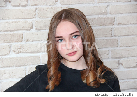 girl with lush hairstyle posing on brick wall background. Girl in black dress 133186195