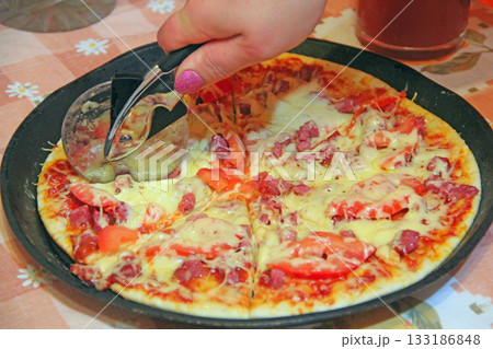 Hand with round roller knife cuts delicious pizza 133186848