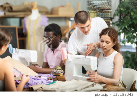 Guy assisting female classmate with threading machine in sewing workshop 133188342