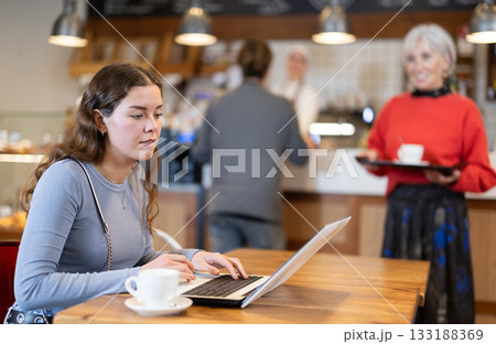 Female freelancer sitting at table in cafe with cup of coffee and laptop, browsing websites on internet Female freelancer sitting at table in cafe with cup of coffee and laptop, browsing websites on internet 133188369