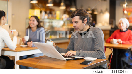 Middle aged man sitting at table, using laptop and enjoing cup of tea in coffee house. Modern lifestyle concept Middle aged man sitting at table, using laptop and enjoing cup of tea in coffee house. Modern lifestyle concept 133188452