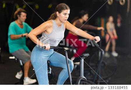 Sportive young girl doing air bike exercises in well-equipped gym Sportive young girl doing air bike exercises in well-equipped gym 133188455