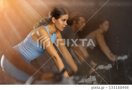 Sportive young girl doing spin bike exercises in well-equipped gym Sportive young girl doing spin bike exercises in well-equipped gym 133188498