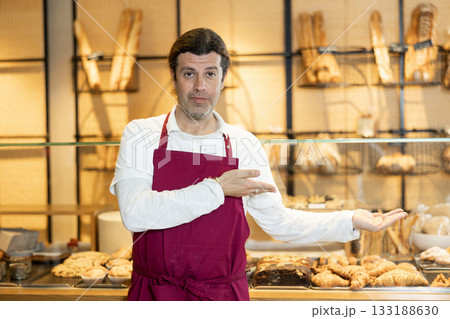 Interested successful baker in maroon apron inviting to bakeshop 133188630