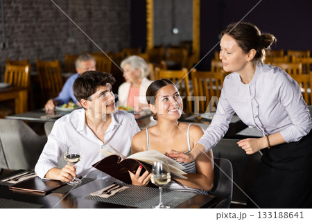 Waitress helps to sort out menu, choose original dish to young married couple 133188641