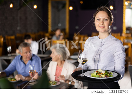 Smiling female owner of restaurant standing with serving tray 133188703