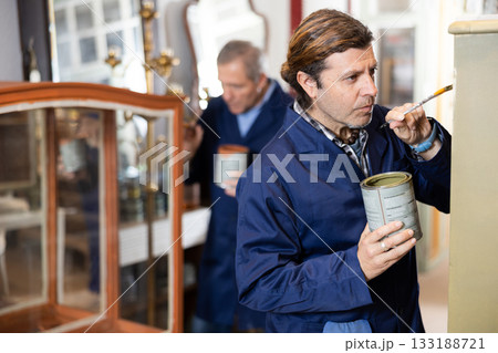 Professional furniture male restorer renewing vintage chest of drawers in workshop 133188721