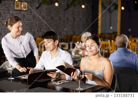 Female owner of restaurant offering dishes from menu to young couple 133188731