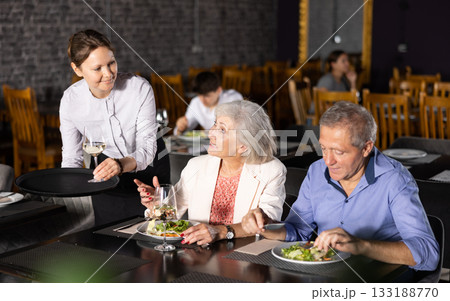 Female waiter serving wine to elderly couple in restaurant 133188770