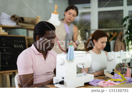 Black man working at machine during group practical sewing course Black man working at machine during group practical sewing course 133188781