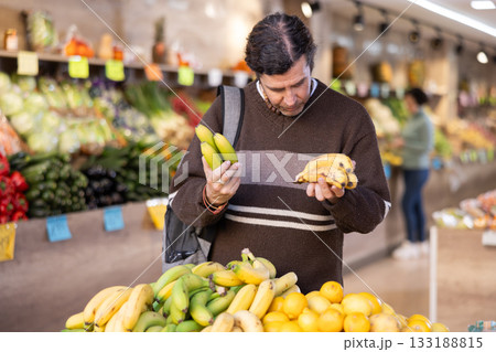 Male shopper carefully selects fresh bananas in grocery supermarket 133188815
