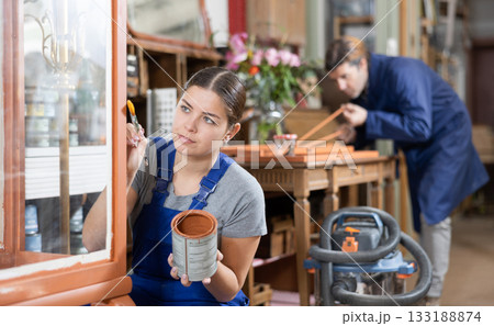 Professional furniture restorer renewing vintage chest of drawers in workshop 133188874