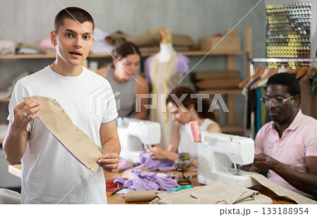 Guy participant present fabric billet, others sewing and working in background 133188954