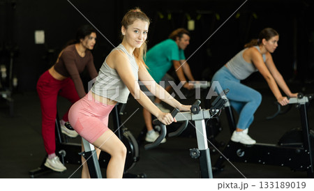 Positive young girl doing spin bike exercises in well-equipped gym Positive young girl doing spin bike exercises in well-equipped gym 133189019