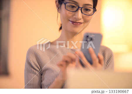 リビングで仕事をしながらスマホを見るミドル女性 133190667