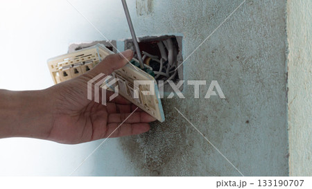 Hand of maintenance people use screwdriver unplug light switch. Socket of switch and power plug take off from outlet wall of house. 133190707