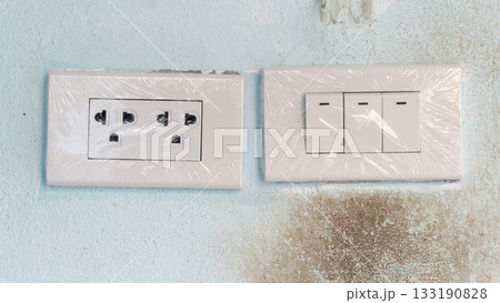 New electric plug three port with light switch three button. Cover confirm for new  wrapped in plastic. On old cement wall blue color with stains. 133190828