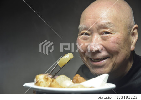 湯気の立ち昇るおでんを食べる笑顔の老人 133191223
