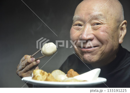 湯気の立ち昇るおでんを食べる笑顔の老人 133191225