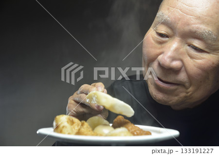 湯気の立ち昇るおでんを食べる笑顔の老人 133191227
