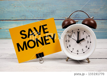 Save Money text written on paper card with alarm clock on wooden background Save Money text written on paper card with alarm clock on wooden background 133191770