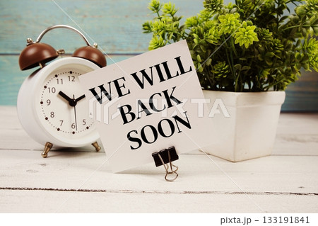 We will back soon text written on paper card with alarm clock on wooden background We will back soon text written on paper card with alarm clock on wooden background 133191841