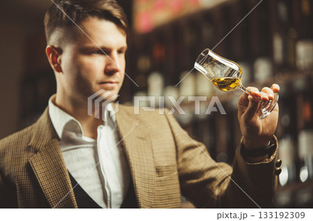 Sommelier holding a glass of whiskey, evaluates the color, smell and taste of alcoholic beverage. Sommelier holding a glass of whiskey, evaluates the color, smell and taste of alcoholic beverage. 133192309