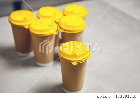 Six Takeaway Coffee Cups With Vibrant Yellow Lids Arranged on Counter 133192319