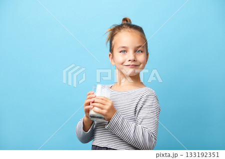 Beautiful little girl with glass of milk, stands on blue isolated. Beautiful little girl with glass of milk, stands on blue isolated. 133192351