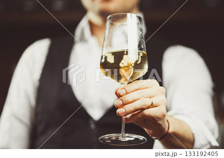 Bartender at the bar hands the camera a glass of white wine, close-up. 133192405