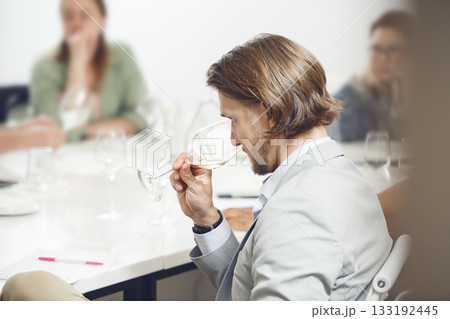 Professional looking sommelier tasting white wine from glass, analysing its taste, color, smell and acidity level. Wine expert studies wine geographic and area on winemaking lecture.  133192445
